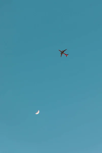 Plane and crescent moon close together on the turquoise sky with copy space