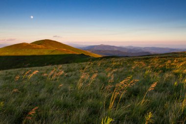 Gün batımında dağ manzarası. Akşam ışığında dağların yamaçlarında. Akşam gökyüzünde ay dağların üzerinde.