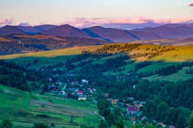 Gün batımında dağlardaki köyün yaz manzarası ve arka planda bir dağ sırası. Gün batımında dağların yamaçları ve tepeler.