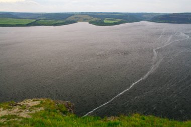 Nehir manzarası ve arka planda yeşil tepeler ve çayırlar. Dik kıyıları ve yeşil çayırları olan geniş bir nehrin ağzı..