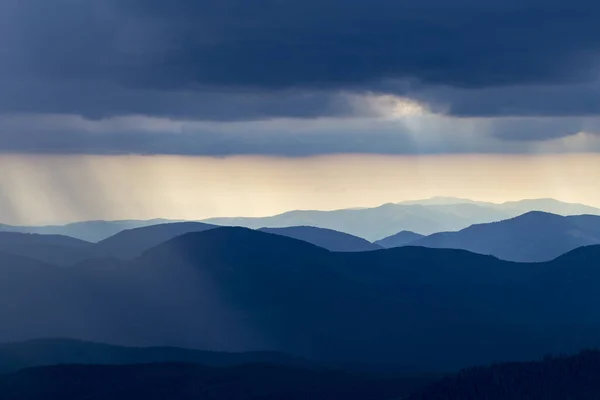 Rain over the mountains against the backdrop of foggy mountain ranges and a cloudy sky. View of the rain clouds over the wooded mountains. Carpathian, Ukraine, Europe.