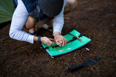Bir adam ateş yakmak için çakmak yakar. Yağmurdan sonra nemli bir ormanda turistler odun parçaları yakar. Vahşi doğada aktif bir eğlence.