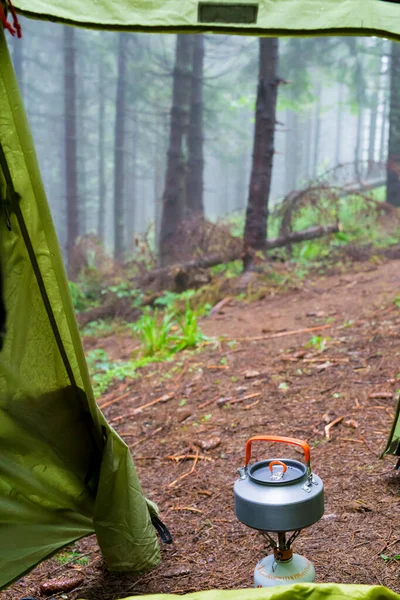 Gas burner with a tourist kettle near a tourist tent on a background of foggy coniferous forest in the mountains. Outdoor tourism — Stock Photo, Image