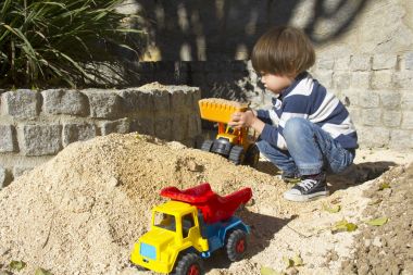 bir kazıcı ve damperli kamyon kum oynarken küçük üç yıl yaşlı erkek çocuk.