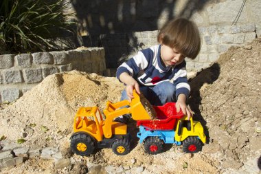 bir kazıcı ve damperli kamyon kum oynarken küçük üç yıl yaşlı erkek çocuk.