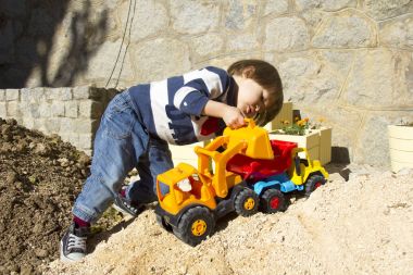 bir kazıcı ve damperli kamyon kum oynarken küçük üç yıl yaşlı erkek çocuk.