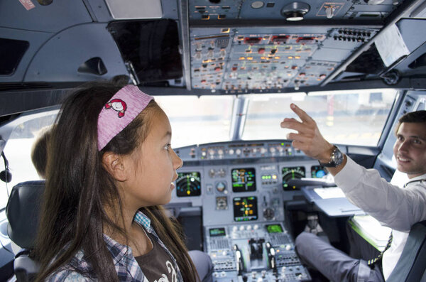Portugal, Algarve, Faro. Circa 10th July 2013. Picture of little girl in tap airline commercial airplane cockpit with Pilot reaching out for controls. 