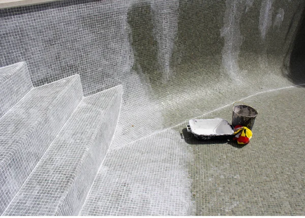 Grouting mosaic tiles in progress on a leaky swimming pool.