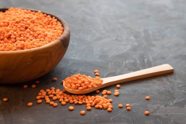 Ahşap bir kase dolusu çiğ kırmızı mercimek ve arka planda mercimek taneleriyle dolu tahta bir kaşık. Metin için yer