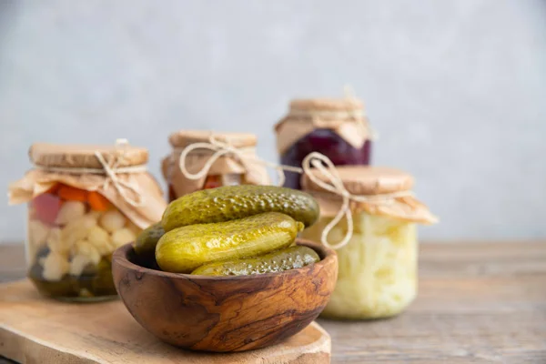 Fermentowane, marynowane, marynowane ogórki z bliska w drewnianej okrągłej misce. W tle preparaty roślinne na zimę w szklanych słoikach — Zdjęcie stockowe