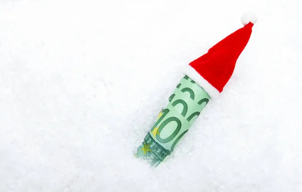 Un rotolo di banconote di 100 euro in un berretto di Babbo Natale di Capodanno giace nella neve bianca. Posto per testo — Foto Stock