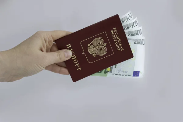 Мужская рука держит заграничный паспорт Российской Федерации с банкнотами 100 евро внутри на светлом фоне. Путешествия. Крупный план — стоковое фото