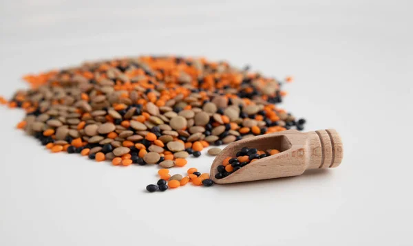 Una manciata di lenticchie di diverse varietà con uno scoop di legno nelle vicinanze su uno sfondo leggero. Lenticchie rosse, marroni e arancioni. Legumi — Foto Stock
