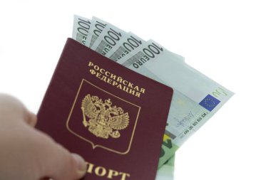 Rus pasaportunun yakın plan resmi içinde euro banknotları olan beyaz bir arka plan üzerinde dikkati dağılmış bir erkek eli var.