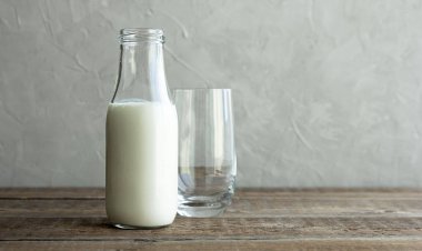 İçinde kefir, süt ya da ev yapımı taze yoğurt bulunan cam bir şişe kırsal bir masada duruyor ve yanında boş bir cam bardak var. Kefir sağlıklı bir atıştırmalıktır ve prebiyotik açısından zengindir..