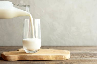 Kefir, süt veya Türk Ayran içeceği bir şişeden cam bardağa dökülüyor. Kırsal bir ahşap masadaki ahşap bir standın üzerinde bir cam duruyor. Metin için yer