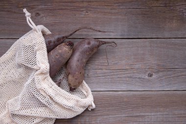 Pamuk, tekrar kullanılabilir bej rengi bir torba içinde taze, uzun soluklu biyo pancarlar ahşap bir masada yatıyor. Plastiğin reddi. Ziyan yok. Metin için yer
