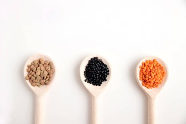 Farklı türde mercimeği olan üç tahta kaşık, beyaz arka planda turuncu, siyah ve kahverengi. Metin için yer