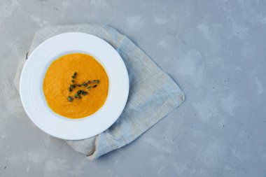 Beyaz seramik tabakla balkabağı çorbası püresi keten bej bir peçeteyle beton gri arka planda. Boşluğu kopyala