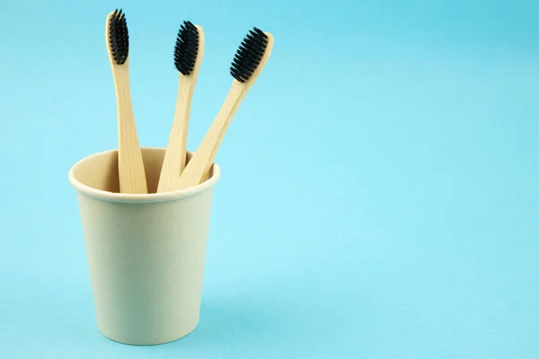 Natural eco bamboo toothbrushes in a bamboo cup stand on a blue background. Save the space. Refusal of plastic. Caring for the ecology of the planet. Zero waste concept. — Stock Photo, Image