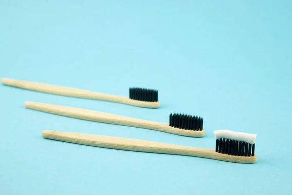 Three toothbrushes from environmentally friendly products recycled lie on a blue background with white organic paste on them. Zero waste. Caring for the ecology of the planet. Oral care — Stock Photo, Image