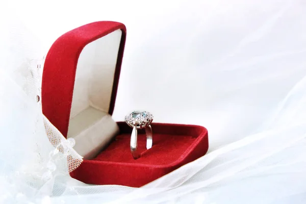 Una caja de terciopelo rojo con un anillo de compromiso, de oro blanco y piedras preciosas se encuentra sobre un velo blanco. Amor. Creación de una familia. Boda. Propuesta de matrimonio . — Foto de Stock