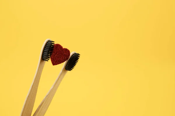 Two bamboo eco brushes and a red heart on a yellow background. Place for text. Oral care, no caries. — Stock Photo, Image