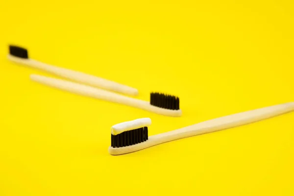 Three bamboo brushes with natural bristles and elodogic toothpaste on a yellow background. Caring for the environment. Zero waste. Proper oral care — Stock Photo, Image
