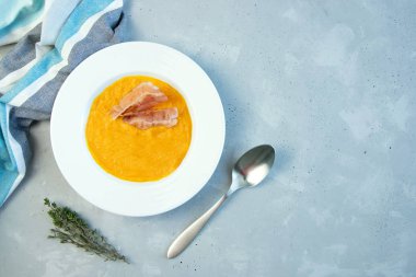 Beton zeminde beyaz bir tabakta pastırmalı balkabağı çorbası. Yakınlarda bir kaşık ve kekik var. Metin için yer.