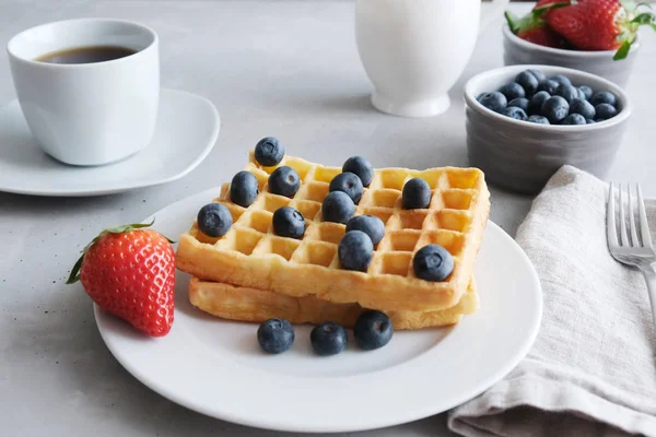 Frische hausgemachte Wiener oder belgische Waffeln mit Blaubeeren und Erdbeeren auf einem weißen Teller. Frühstück mit Waffeln mit Beeren und einer Tasse Kaffee. — Stockfoto