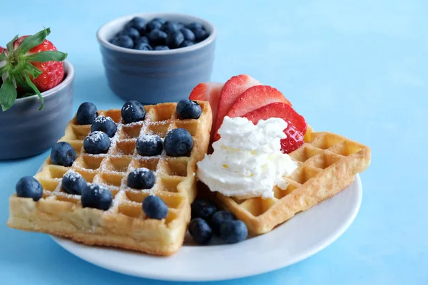 Biyolojik çilek, yabanmersini ve mavi arka planda krem şantili taze Viyana ev yapımı waffle 'lar. Arka planda fincanlar, taze böğürtlenli kaseler var. Kahvaltı, tatlı. Boşluğu kopyala