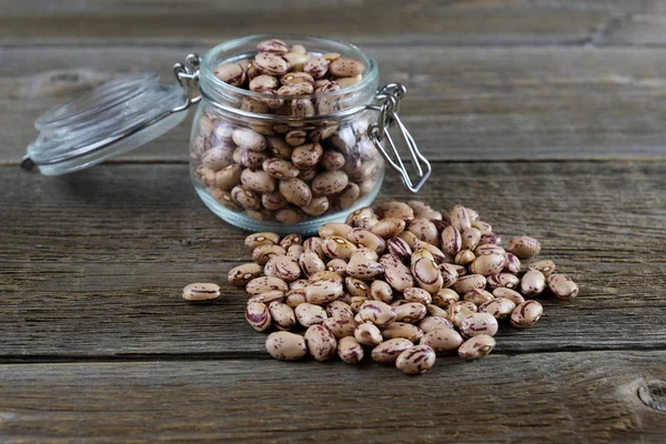 Frijoles pardos pinto con manchas en un frasco de vidrio y frijoles están dispersos cerca en una vieja mesa de madera. legumbres como fuente de proteínas y fitaminas . — Foto de Stock