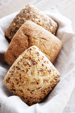 Bej bir peçeteye farklı türde kahvaltı ruloları. Çavdar, tam tahıl ve tohumlu buğday ekmeği. Kahvaltıda. Dikey oryantasyon. Fırın.