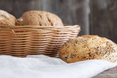 Hasır sepetin içinde taze pişmiş çörekler ve ahşap bir arka planda yanında bir çörek. Ev yapımı ekmek. Fırında ekmek var. Fırın ürünleri.