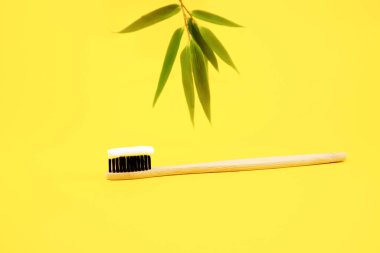Beyaz diş macunlu doğal çevre dostu kıllara sahip bambu doğal bir fırça sarı arka planda ve arka plandaki bambu yapraklarında bulunur. Geri dönüşüm ürünleri. Ağız bakımı. Boşluğu kopyala.
