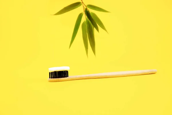 A bamboo natural brush with natural eco-friendly bristles with white toothpaste lies on a yellow background and in the background bamboo leaves. Recycling products. Oral care. Copy space.