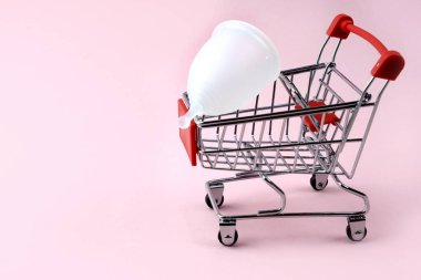 Beyaz silikon bir adet kupası bir alışveriş arabasında yatıyor. Kritik günlerde koruma. Kadınlar için yenilik. Pembe arka plan. Metin için yer.