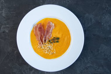 Balkabağı çorbası, domuz pastırması, biberiye filizi ve kenevir tohumlarıyla süslenmiş bir tabağın yakın çekimi..