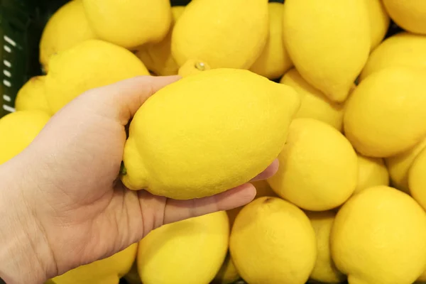 Färsk Gul Citron Kvinnlig Hand Mot Bakgrund Hög Med Citroner — Stockfoto