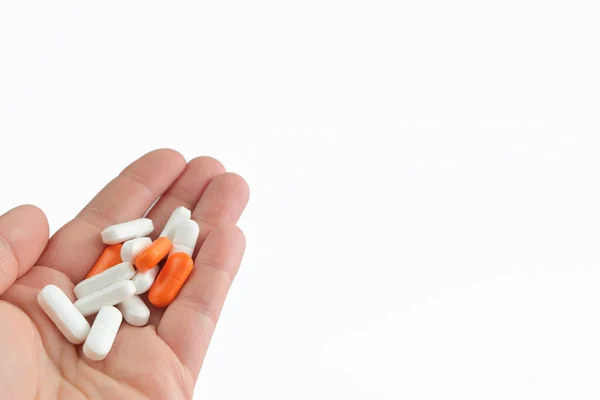 Close-up of a hand on the palm of which lies white and orange pills, pills, drugs on a white background. Medical concept. Copy space. — Stock Photo, Image