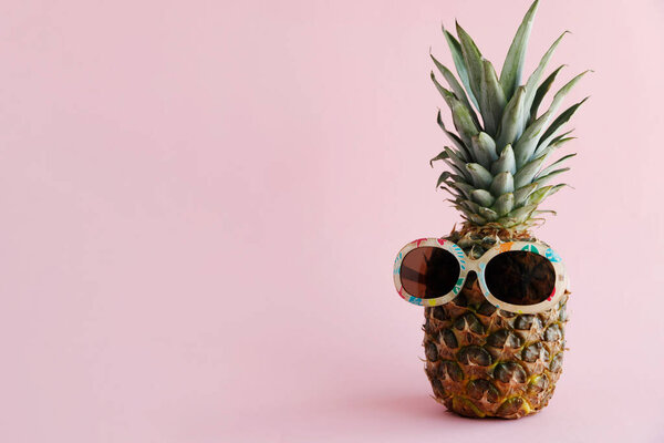 Fresh pineapple in sunglasses stands on a pink background. The concept of rest, travel, vacation, relaxation. Save the space. Horizontal orientation.