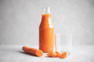 Yanında taze havuç suyu ve boş bir bardak olan bir şişe. Ön planda bir havuç var. Gri arka plan. Metin için yer.