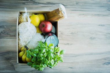 İçinde çeşitli malzemeler, tahıllar, konserve yiyecekler, makarna, muz ve elmalar olan karton bir kutu. Metin için yer.