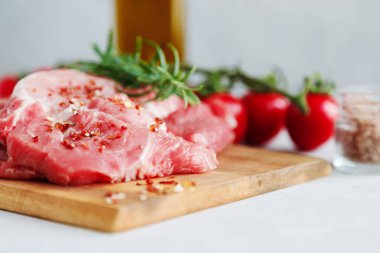 Pişmemiş domuz eti, baharat ve biberiye filizleri. Arka planda vişneli domatesler var.