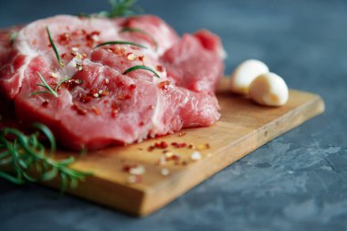 Taze domuz bifteği, baharat serpilmiş pirzola ve ahşap kesme tahtasına biberiye serpiştirilmiş ve bir sıra sarımsaklı karanfil. Karanlık arka plan. Metin için yer