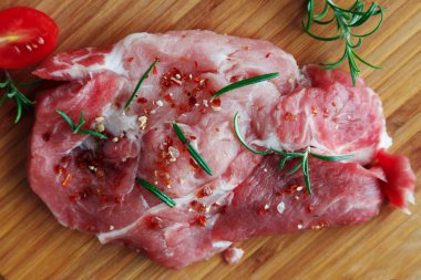 Baharatlı taze domuz bifteği ve ahşap bir tahtanın üzerinde biberiye yaprakları..