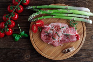 Taze yeşil kuşkonmaz ve vişneli domatesle ahşap bir masada baharatlı domuz pirzolası. Izgara sebze ve et..