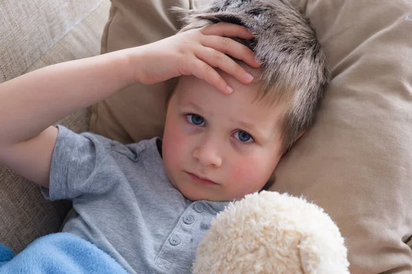 Un petit garçon malade s'allonge sur un oreiller et mesure la température sur son front avec sa main. Grippe . — Photo