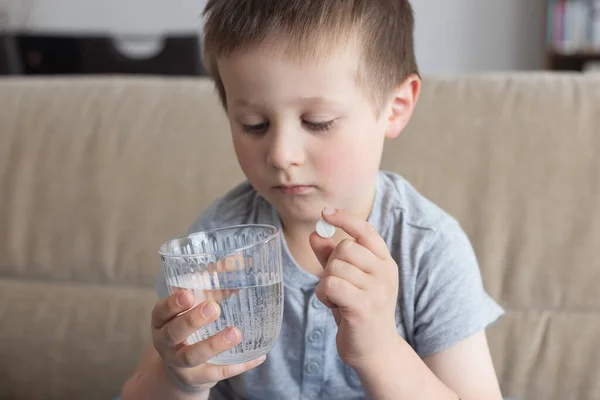 Le petit garçon ne veut pas boire de médicaments. Enfant avec un comprimé et un verre d'eau. Prendre des vitamines, des antibiotiques, des médicaments — Photo