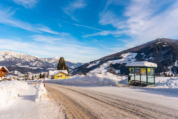 Fermata autobus austriaca, cartello comprensorio sciistico Schladming-Dachstein, Intorno alla strada innevata, alberi e montagne . — Foto Stock